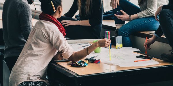Four people are gathered around a table and seem to be discussing something. On the table there is paper and pens.